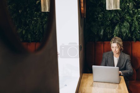 Téléchargez les photos : Femme d'affaires mature administrateur de restaurant assis et travaillant sur ordinateur portable - en image libre de droit
