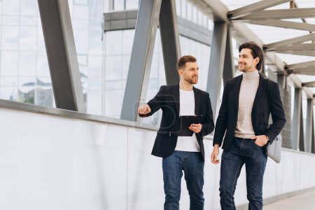 Foto de Dos modernos empresarios felices cruzando un puente de la ciudad discutiendo algo en el contexto de oficinas urbanas y edificios - Imagen libre de derechos