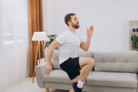 Photo for Handsome bearded man doing hamstring stretch exercise at home. - Royalty Free Image