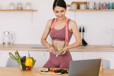 Photo for Portrait of happy sporty woman blogger making asparagus cooking and leading video conference on healthy eating topic on laptop in kitchen - Royalty Free Image
