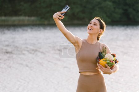 Photo for Happy sporty woman taking selfie with plate of fresh vegetables on the outdoors - Royalty Free Image