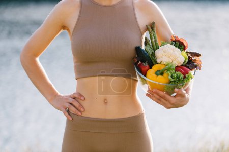 Foto de Placa vegana femenina de verduras frescas cerca del vientre al aire libre - Imagen libre de derechos