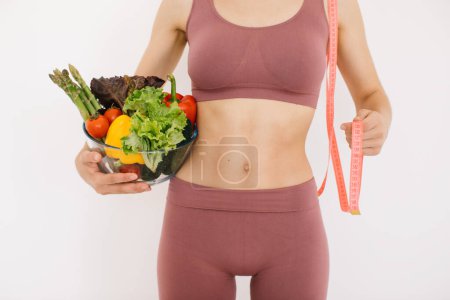 Téléchargez les photos : Jeune femme heureuse tenant une assiette avec différents légumes et une règle sur un fond blanc - en image libre de droit