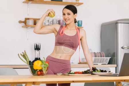 Téléchargez les photos : Portrait de femme sportive heureuse tenant pomme fraîche et montrant biceps dans la cuisine, concept de saine alimentation - en image libre de droit