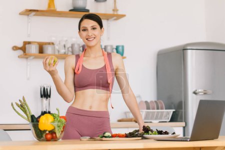 Foto de Retrato de mujer deportiva feliz sosteniendo manzana fresca y mostrando bíceps en la cocina, concepto de alimentación saludable - Imagen libre de derechos