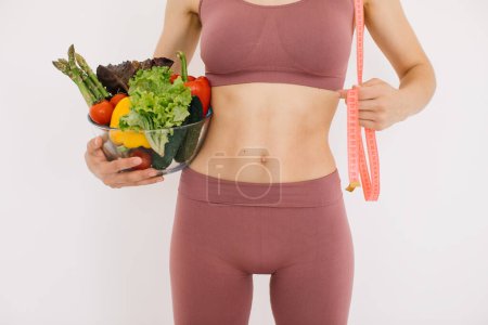 Téléchargez les photos : Jeune femme heureuse tenant une assiette avec différents légumes et une règle sur un fond blanc - en image libre de droit