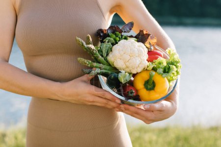 Foto de Placa vegana femenina de verduras frescas cerca del vientre al aire libre - Imagen libre de derechos