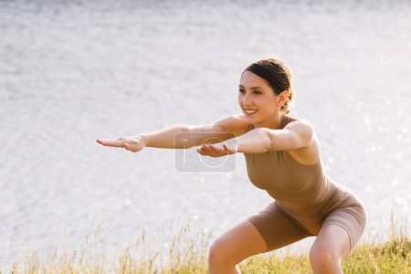 Téléchargez les photos : Femme heureuse pratiquant le yoga en plein air près de la rivière - en image libre de droit