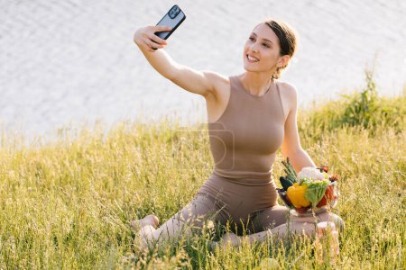 Téléchargez les photos : Heureuse femme sportive prenant selfie avec assiette de légumes frais en plein air - en image libre de droit