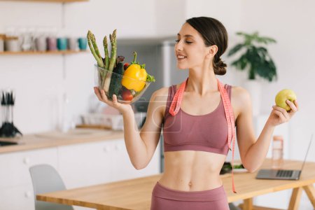 Portrait of happy sporty woman holding apple and plate of fresh vegetables, healthy eating concept