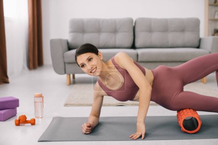 Téléchargez les photos : Attrayant jeune femme sportive faisant des exercices sur l'abdomen avec un rouleau à la maison. - en image libre de droit