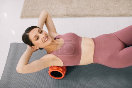 Foto de Atractiva joven mujer deportiva haciendo ejercicios en el abdomen con un rodillo en casa. - Imagen libre de derechos