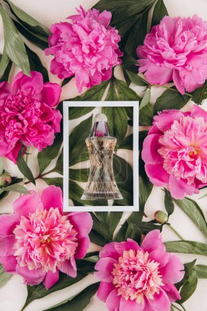 Foto de Perfume en un marco blanco con peonías sobre fondo pastel. Prepárate. Concepto de moda. - Imagen libre de derechos