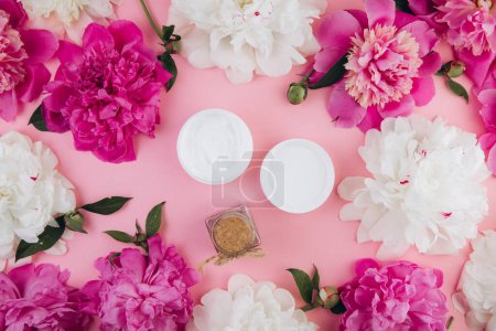 Téléchargez les photos : Un masque crème et une bouteille de sel de mer sur un fond rose clair avec une délicate fleur de pivoine. Image maquillée. - en image libre de droit