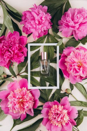 Foto de Perfume en un marco blanco con peonías sobre fondo pastel. Prepárate. Concepto de moda. - Imagen libre de derechos
