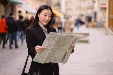 Téléchargez les photos : Portrait d'une belle Coréenne tenant une carte dans les rues d'une vieille ville européenne. Femme asiatique touriste ou d'affaires dame voyageant en Europe. - en image libre de droit
