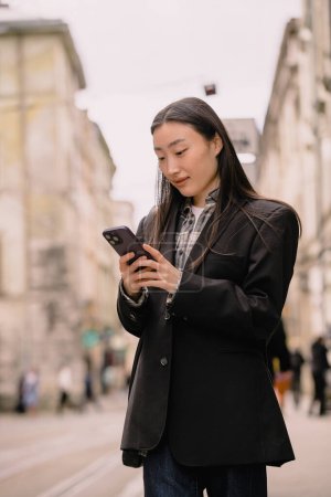 Téléchargez les photos : Jeune femme d'affaires asiatique couronnée de succès occupé belle, coréen femme d'affaires professionnelle tenant téléphone portable en utilisant smartphone debout ou marcher sur la rue de la vieille ville à l'extérieur. - en image libre de droit