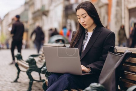 Foto de Negocio freelance joven adulto asiático mujer utilizando ordenador portátil para el trabajo. Sentado al aire libre en el día. Vida urbana con tecnología moderna. - Imagen libre de derechos