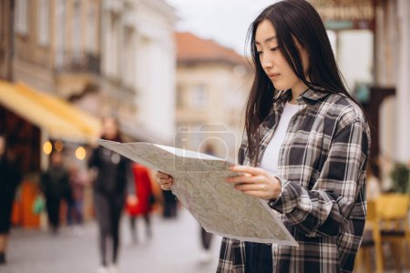 Foto de Retrato de una hermosa morena coreana sosteniendo un mapa en las calles de la ciudad vieja. Mujer asiática turista o dama de negocios viajando en Europa. - Imagen libre de derechos