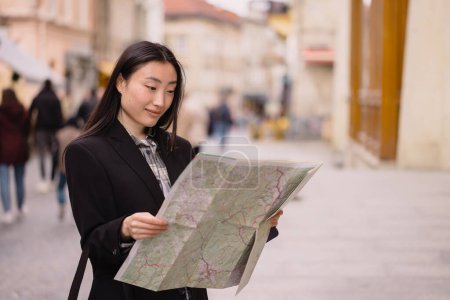Foto de Retrato de una hermosa mujer coreana sosteniendo un mapa en las calles de una antigua ciudad europea. Mujer asiática turista o dama de negocios viajando en Europa. - Imagen libre de derechos