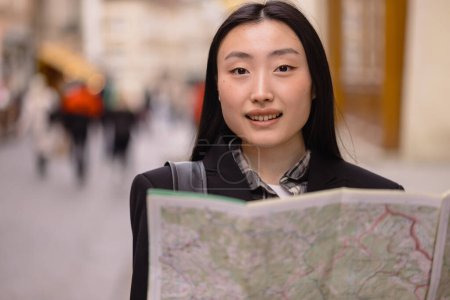 Téléchargez les photos : Portrait d'une belle Coréenne tenant une carte dans les rues d'une vieille ville européenne. Femme asiatique touriste ou d'affaires dame voyageant en Europe. - en image libre de droit