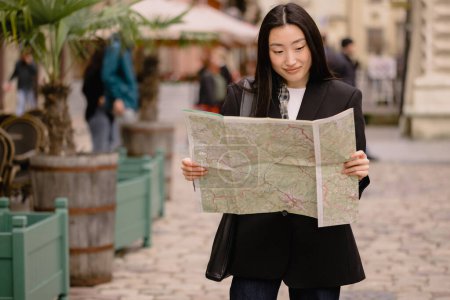 Photo for Portrait young asian woman tourist in casual clothes on old city street in europe while checking direction on map - Royalty Free Image