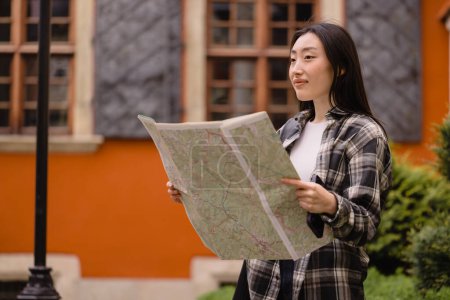 Foto de Retrato de una hermosa morena feliz mujer coreana sosteniendo un mapa en las calles de la ciudad vieja. Mujer asiática turista viajando por Europa. - Imagen libre de derechos