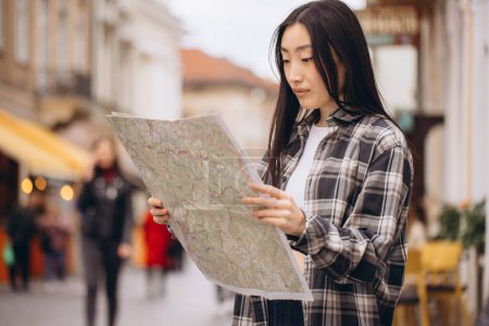 Foto de Retrato de una hermosa morena coreana sosteniendo un mapa en las calles de la ciudad vieja. Mujer asiática turista o dama de negocios viajando en Europa. - Imagen libre de derechos