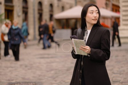 Téléchargez les photos : Portrait jeune femme asiatique heureuse touriste en vêtements décontractés sur la rue de la vieille ville en Europe tout en vérifiant la direction sur la carte et la navigation sur smartphone - en image libre de droit
