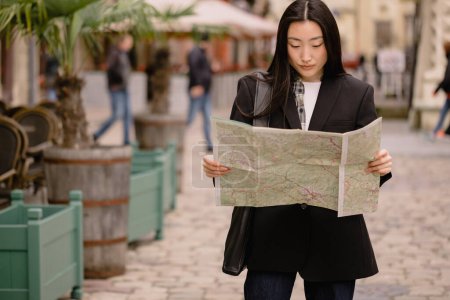 Téléchargez les photos : Portrait jeune femme asiatique touristique en vêtements décontractés sur la rue de la vieille ville en Europe tout en vérifiant la direction sur la carte - en image libre de droit