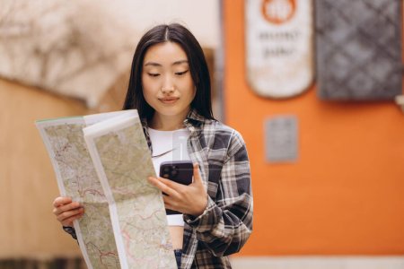 Foto de Retrato de una hermosa morena coreana sosteniendo un mapa y comparándolo con la navegación por las calles del casco antiguo. Mujer turista asiática viajando en Europa. - Imagen libre de derechos