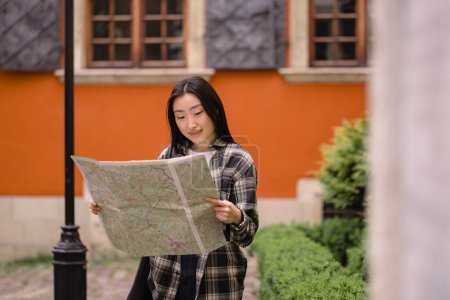 Photo for Portrait of a beautiful happy brunette Korean woman holding a map on the streets of the old city. Asian woman tourist lady traveling in Europe. - Royalty Free Image