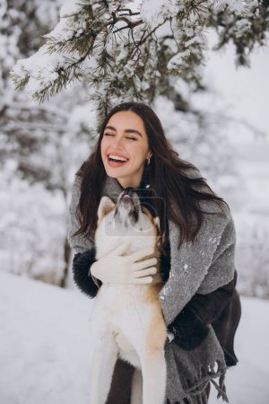 Téléchargez les photos : Jolie femme heureuse passer du temps avec le chien akita inu en hiver dans la forêt enneigée - en image libre de droit