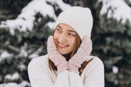 Téléchargez les photos : Portrait d'une belle fille heureuse en tricot blanc posant dans un manteau d'hiver par une journée enneigée - en image libre de droit