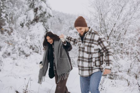 Photo for A young happy and loving couple walking in a snowy forest in the mountains - Royalty Free Image
