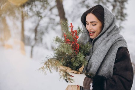 Foto de Feliz bonita mujer sonriente sosteniendo ramo de pino en el bosque nevado en invierno. - Imagen libre de derechos
