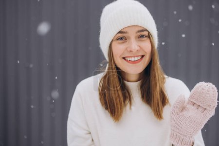 Téléchargez les photos : Joyeux jeune femme en mitaines tricotées saluant par temps neigeux en hiver - en image libre de droit