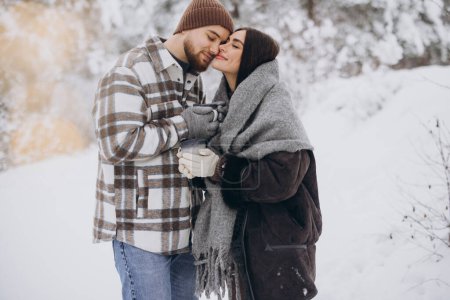 Téléchargez les photos : Heureux beau couple se reposant et buvant du thé chaud dans la forêt en hiver dans les montagnes - en image libre de droit
