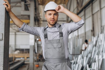 Foto de Retrato de un trabajador feliz con un uniforme gris y un sombrero blanco posando sobre el fondo de la producción de fábrica - Imagen libre de derechos