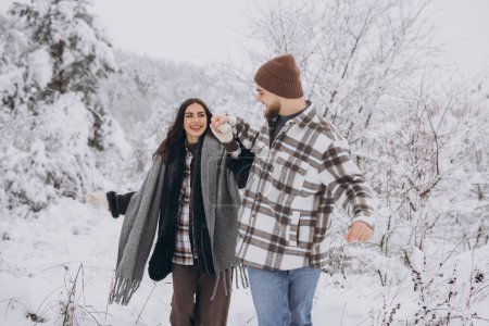 Foto de Una joven pareja feliz y cariñosa caminando en un bosque nevado en las montañas - Imagen libre de derechos
