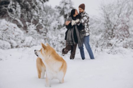 Foto de Feliz pareja joven con un perro akita en el bosque en el día de invierno - Imagen libre de derechos