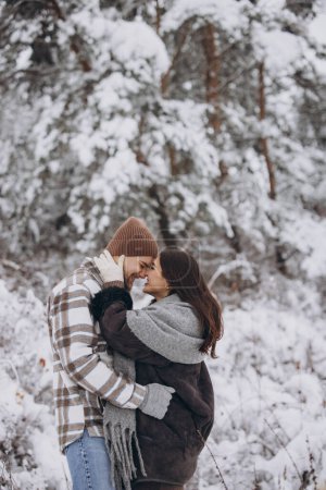 Téléchargez les photos : Un jeune couple heureux et aimant se promène dans une forêt enneigée dans les montagnes - en image libre de droit