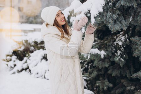Foto de Retrato de una hermosa chica feliz en ropa blanca de punto posando en un abrigo de invierno en un día nevado - Imagen libre de derechos