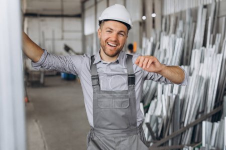 Foto de Retrato de un trabajador feliz con un uniforme gris y un sombrero blanco posando sobre el fondo de la producción de fábrica - Imagen libre de derechos
