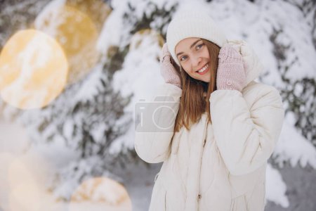 Photo for A happy woman in knitted mittens poses against the background of a snowy pine tree in winter - Royalty Free Image