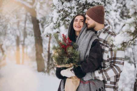 Photo for Cute young couple in love with pine bouquet spending time on Valentine's day in snowy winter forest in mountains - Royalty Free Image