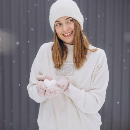 Photo for Happy woman in knitted mittens holding a snow heart on a winter snowy day - Royalty Free Image
