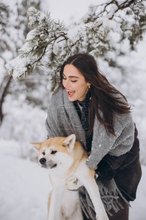 Téléchargez les photos : Jolie femme heureuse passer du temps avec le chien akita inu en hiver dans la forêt enneigée - en image libre de droit
