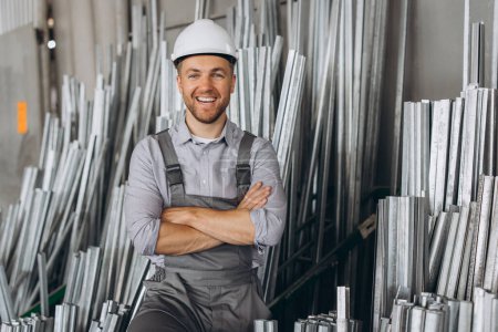 Foto de Trabajador de fábrica masculino barbudo feliz en uniforme especial y sombrero duro blanco que sostiene el marco de aluminio en la producción de ventanas y puertas plásticas del metal - Imagen libre de derechos