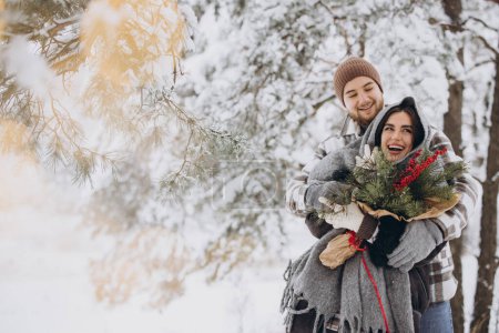 Photo for Cute young couple in love with pine bouquet spending time on Valentine's day in snowy winter forest in mountains - Royalty Free Image